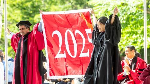 Two people in academic regalia hold up a banner labeled 2025 during the University's Convocation ceremony