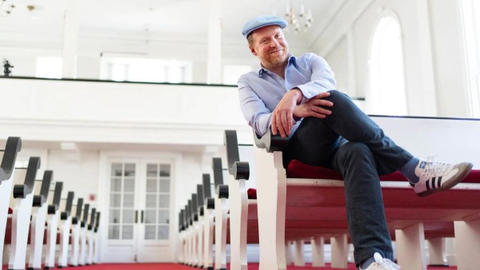 The Rev. Ian White Maher, MDiv '04, sitting in a church pew with legs crossed