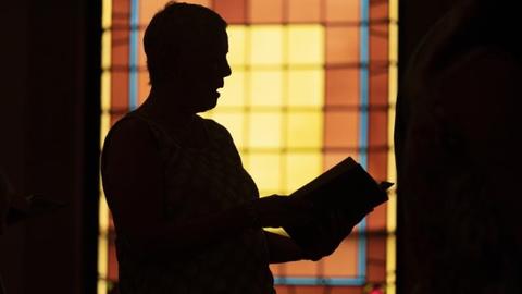 Shadow of man in front of stained glass in Maine church. AP photo
